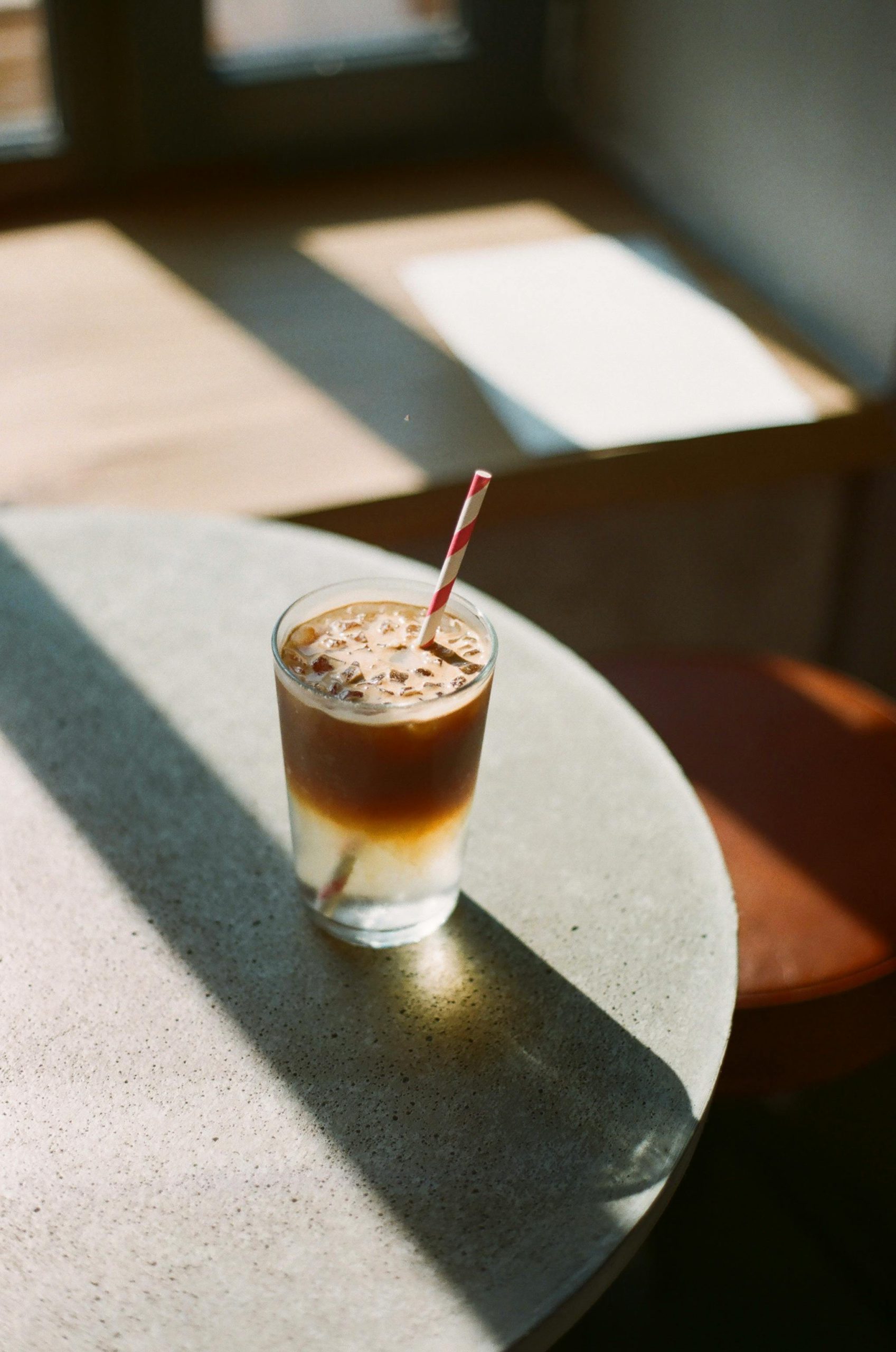 A close-up of a refreshing iced coffee in a glass with a straw, basking in sunlight on a table.